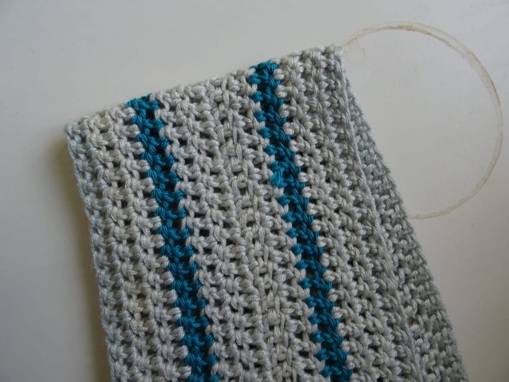 a folded piece of mostly-grey flat crochet on a white desk next to a coffee ring for scale